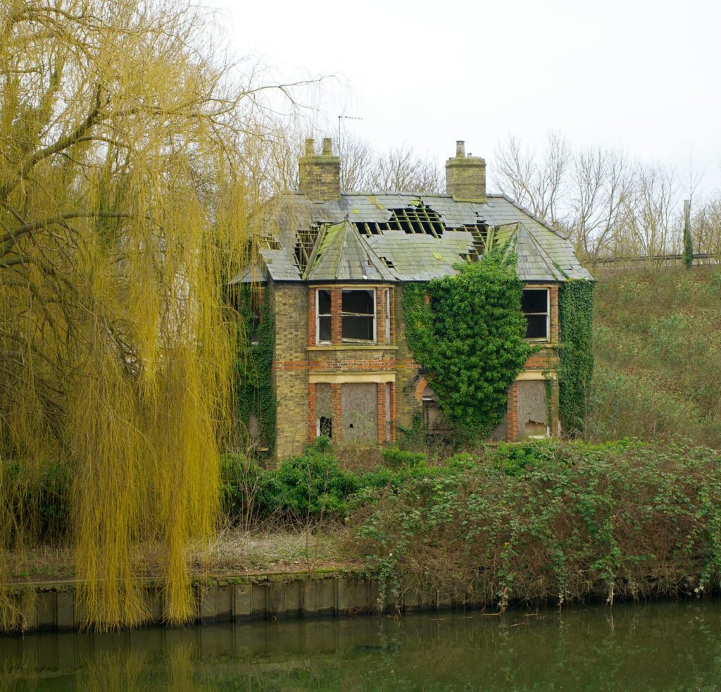 A scenic view of an abandoned house covered in ivy by the river in Godmanchester, England.